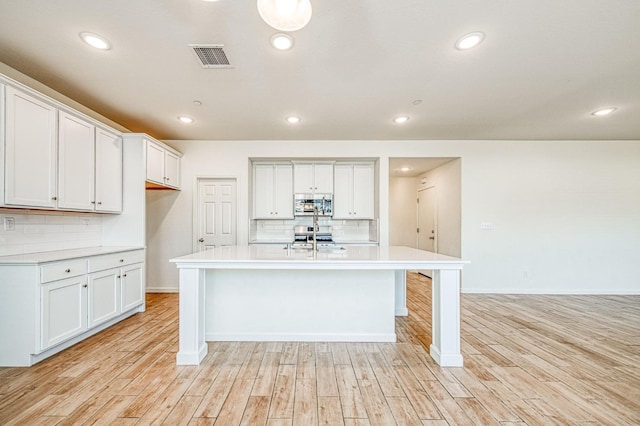 kitchen with tasteful backsplash, white cabinetry, a center island with sink, and light wood-type flooring