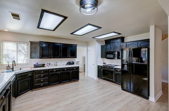 kitchen with tasteful backsplash, sink, stove, light hardwood / wood-style floors, and black fridge