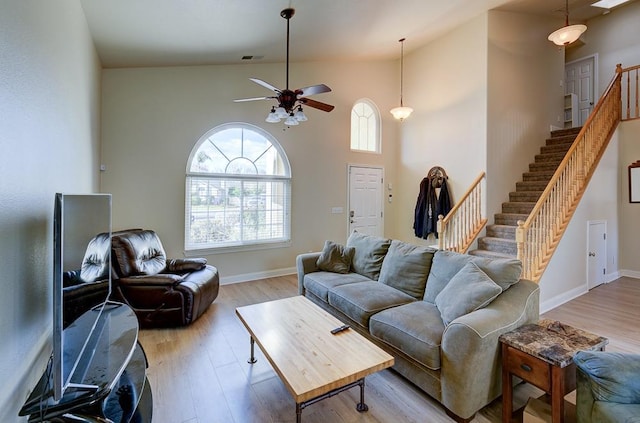 living room featuring light hardwood / wood-style flooring, ceiling fan, and a high ceiling