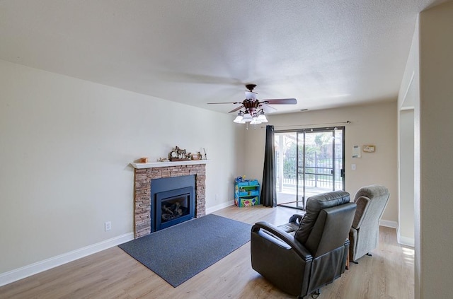 living room with a stone fireplace, light hardwood / wood-style flooring, a textured ceiling, and ceiling fan