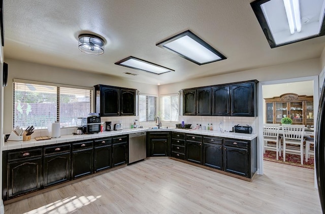 kitchen with tasteful backsplash, dishwasher, sink, and light hardwood / wood-style flooring