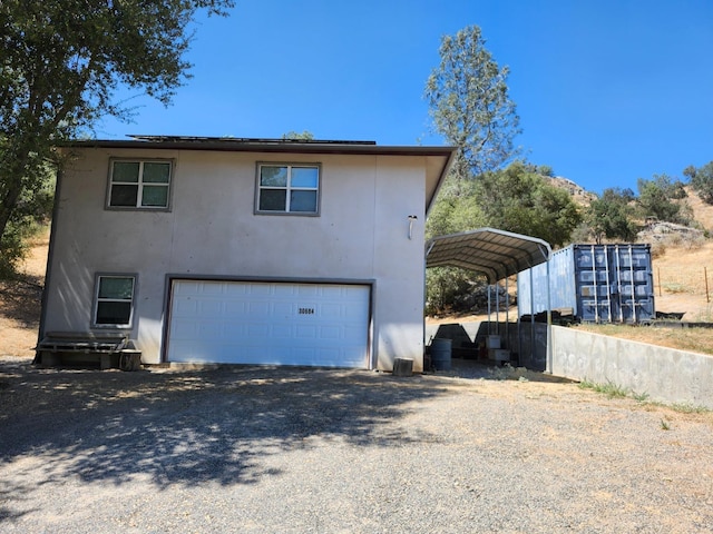 view of home's exterior with gravel driveway, stucco siding, a detached carport, and an attached garage