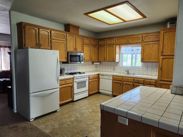 kitchen featuring tasteful backsplash, a sink, white appliances, brown cabinets, and tile countertops