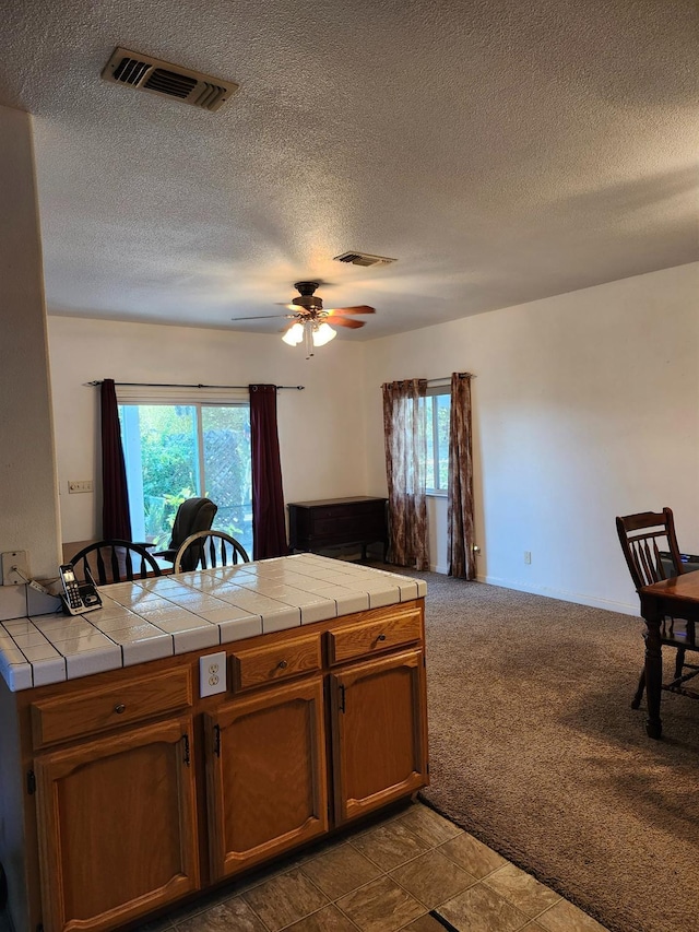 kitchen with a wealth of natural light, tile counters, ceiling fan, and dark carpet