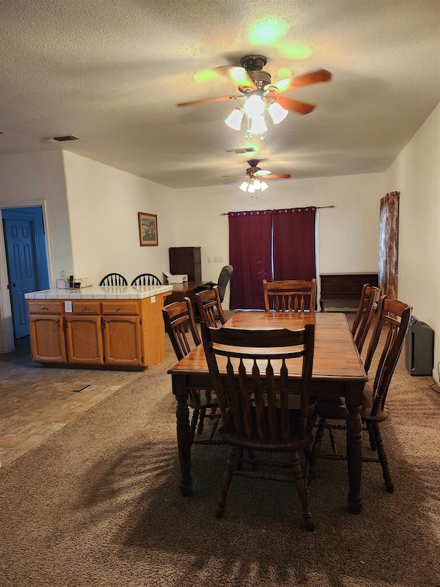 carpeted dining room featuring ceiling fan and a textured ceiling