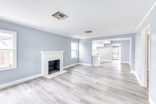 unfurnished living room with a brick fireplace, crown molding, and light hardwood / wood-style floors