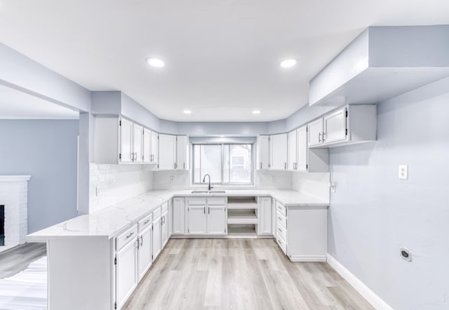 kitchen featuring white cabinetry, sink, decorative backsplash, kitchen peninsula, and a brick fireplace