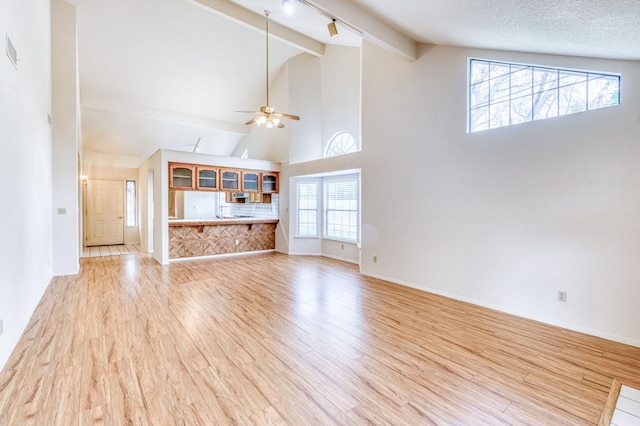 unfurnished living room featuring high vaulted ceiling, a textured ceiling, beamed ceiling, ceiling fan, and light hardwood / wood-style floors