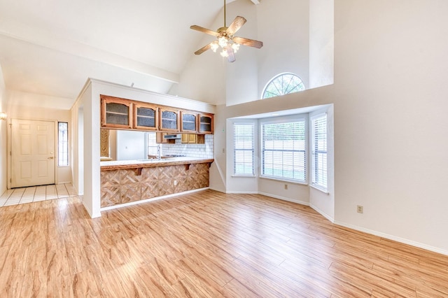 unfurnished living room with sink, light hardwood / wood-style flooring, high vaulted ceiling, and ceiling fan