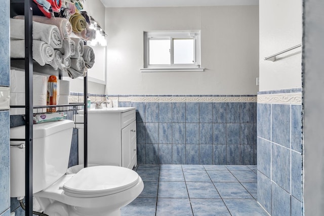 bathroom featuring tile patterned flooring, tile walls, a wainscoted wall, toilet, and vanity