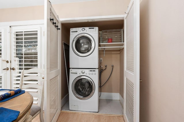 clothes washing area with stacked washer and clothes dryer and light wood-type flooring