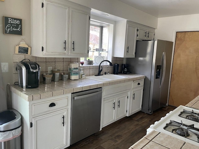 kitchen with sink, tasteful backsplash, tile counters, stainless steel appliances, and white cabinets