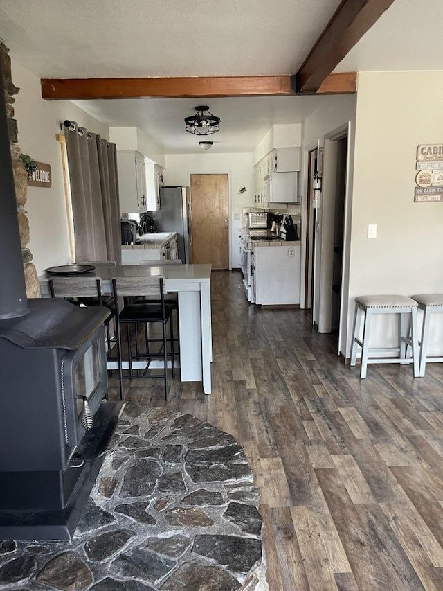 kitchen featuring stainless steel refrigerator, beamed ceiling, a wood stove, and white cabinets