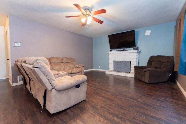 living room featuring ceiling fan, a brick fireplace, dark hardwood / wood-style floors, and a textured ceiling