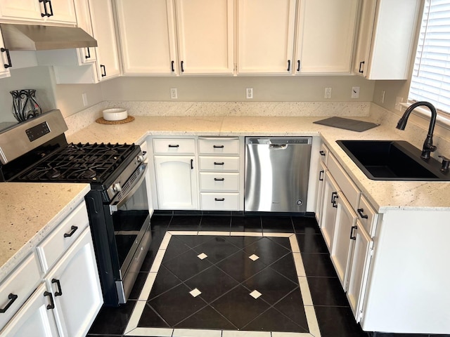 kitchen with sink, white cabinets, dark tile patterned floors, light stone counters, and stainless steel appliances