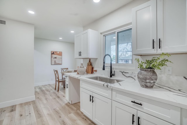 kitchen with white cabinetry, sink, light hardwood / wood-style flooring, and light stone countertops