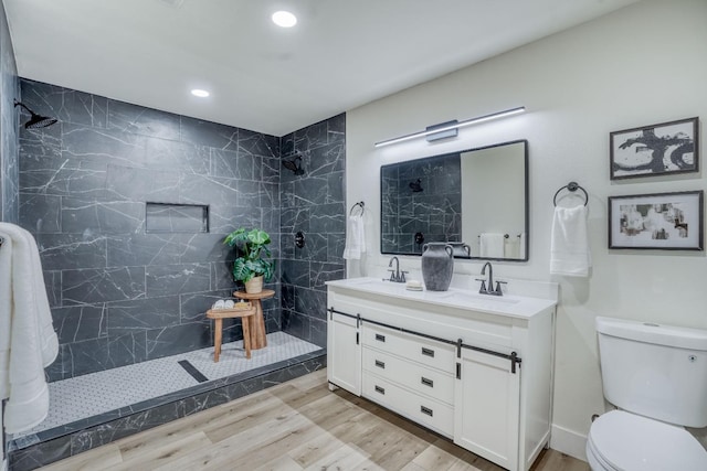 bathroom featuring vanity, hardwood / wood-style flooring, toilet, and tiled shower