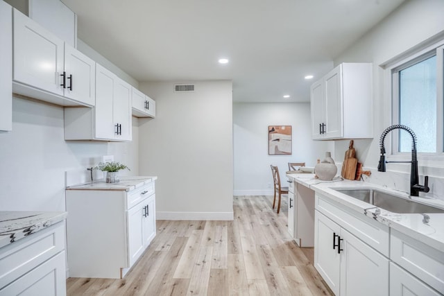 kitchen with white cabinetry, sink, light stone counters, and light hardwood / wood-style flooring