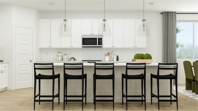 kitchen featuring hanging light fixtures, an island with sink, white cabinets, and a kitchen bar