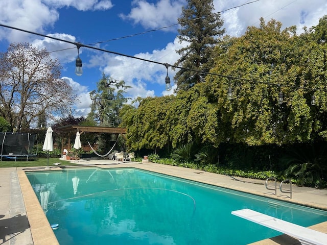 view of swimming pool featuring a trampoline, a pergola, and a diving board