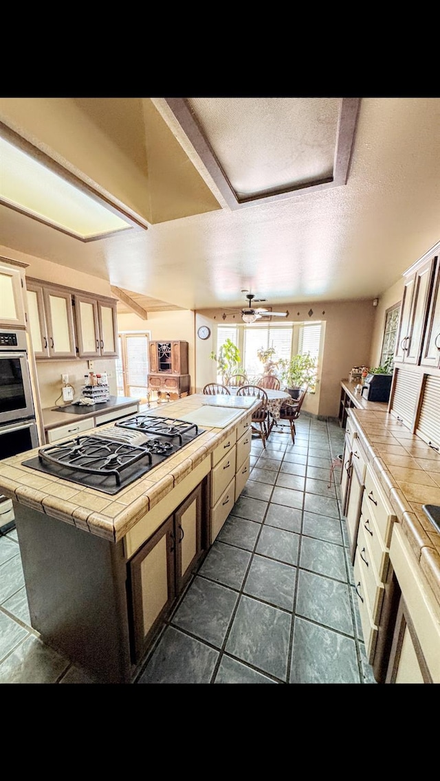 kitchen with a textured ceiling, appliances with stainless steel finishes, tile counters, dark tile patterned flooring, and a kitchen island