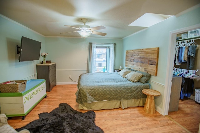 bedroom with a skylight, ornamental molding, a walk in closet, ceiling fan, and light hardwood / wood-style flooring