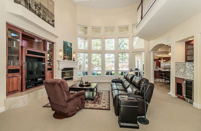 carpeted living room featuring ornate columns, a high ceiling, and beverage cooler