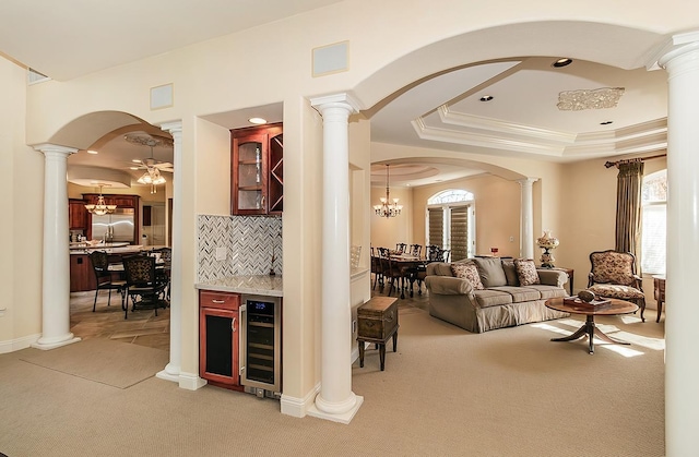 carpeted living room featuring a tray ceiling, beverage cooler, and ornate columns