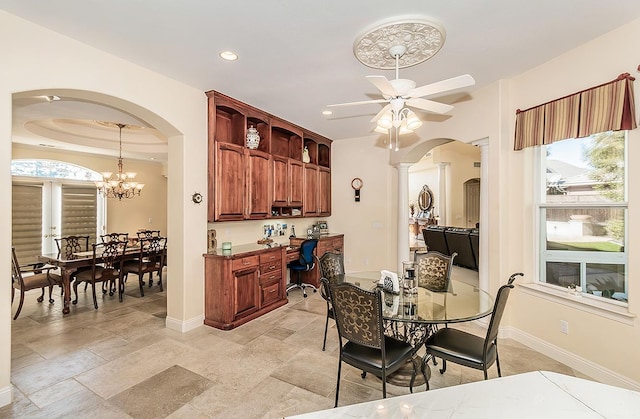 dining space featuring built in desk, ceiling fan with notable chandelier, and a tray ceiling