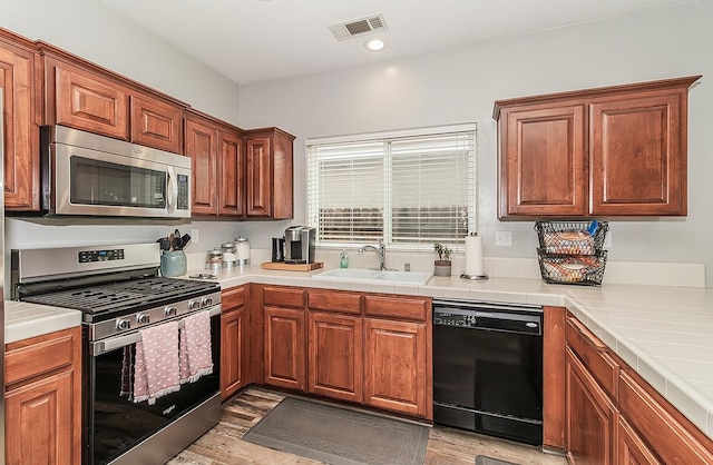 kitchen featuring stainless steel appliances, tile counters, light hardwood / wood-style floors, and sink