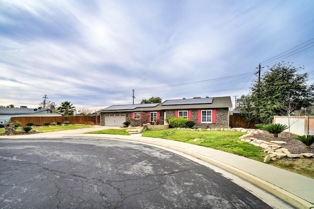 ranch-style home with a garage, a front lawn, and solar panels