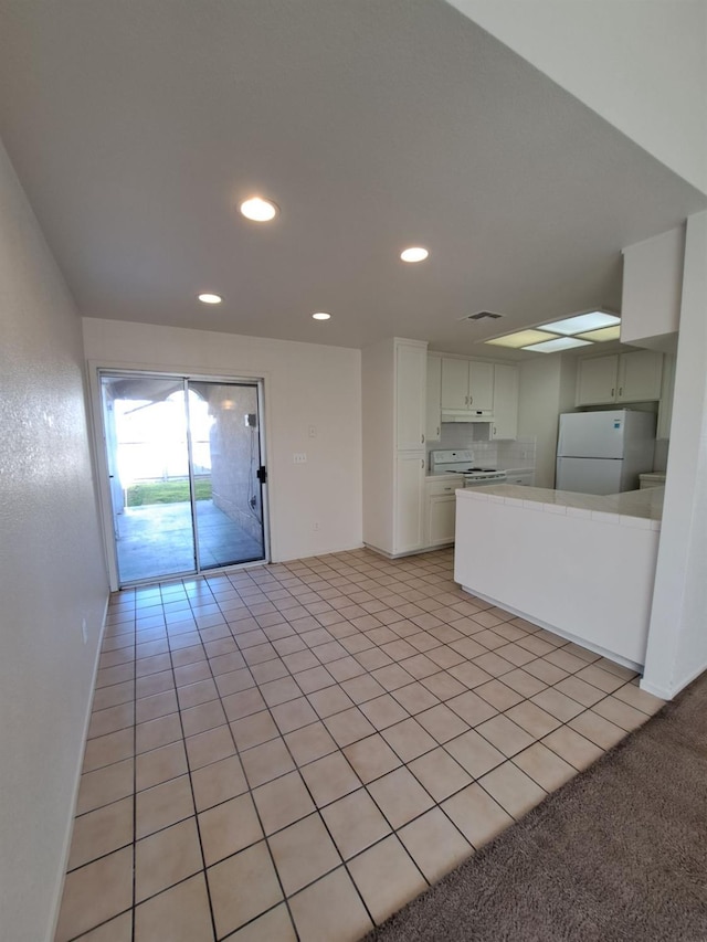 kitchen with white appliances, light tile patterned floors, a peninsula, white cabinetry, and recessed lighting