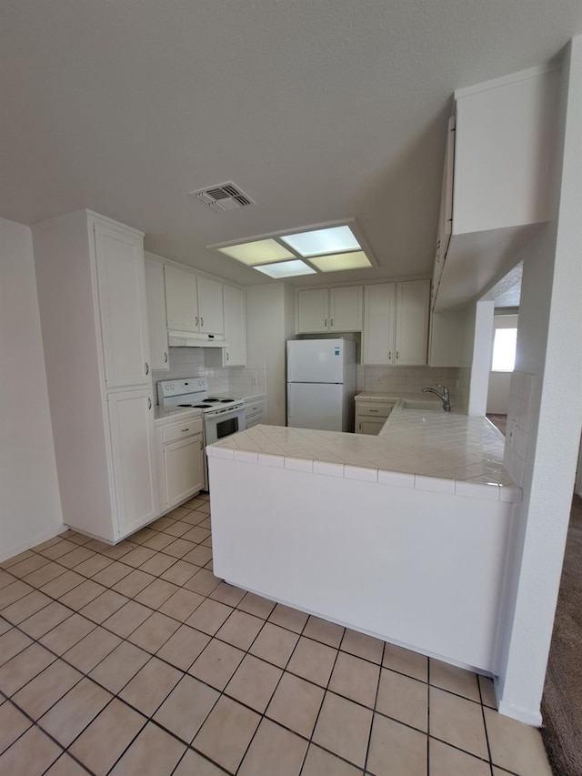 kitchen featuring a peninsula, white appliances, a sink, visible vents, and tile counters