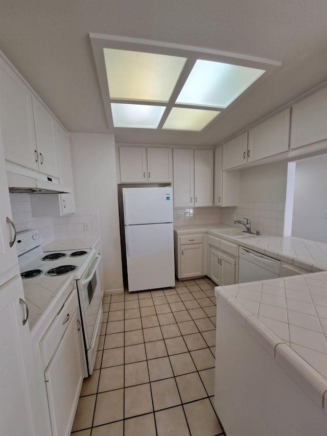 kitchen featuring white appliances, a sink, tile countertops, and under cabinet range hood