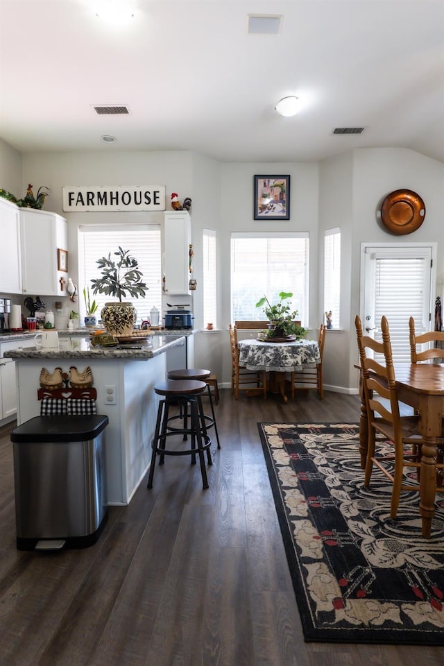 kitchen featuring dark wood-type flooring, a kitchen breakfast bar, dark stone counters, and white cabinets