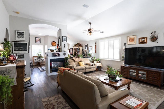 living room featuring a multi sided fireplace, vaulted ceiling, dark wood-type flooring, and ceiling fan