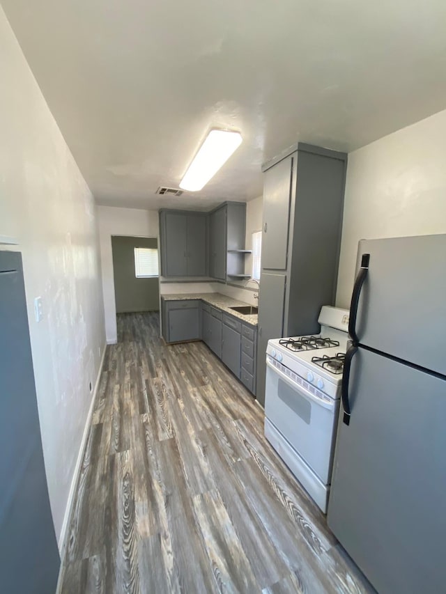 3185 W Mckinley, Fresno, CA 93722 - kitchen with freestanding refrigerator, white range with gas cooktop, visible vents, gray cabinets, and wood finished floors