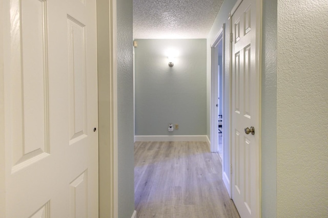 hallway with light hardwood / wood-style flooring and a textured ceiling