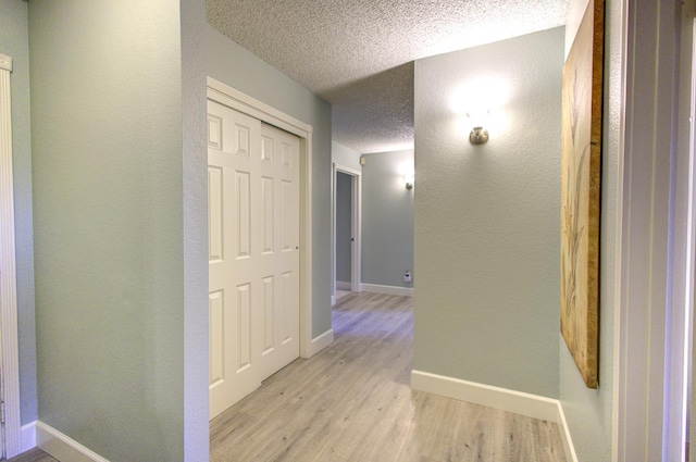 hall with a textured ceiling and light wood-type flooring