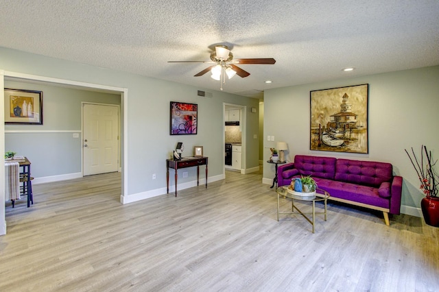 living room with ceiling fan, light hardwood / wood-style floors, and a textured ceiling