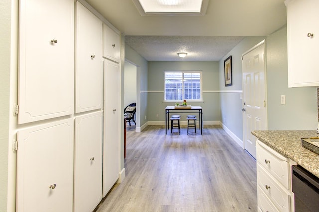 kitchen with light hardwood / wood-style flooring, dishwasher, white cabinetry, light stone countertops, and a textured ceiling