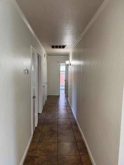 hallway featuring dark tile patterned flooring, crown molding, and a textured ceiling