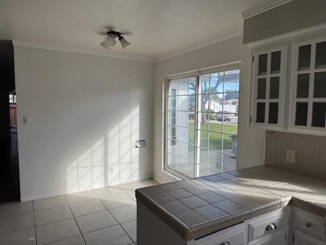 kitchen featuring tasteful backsplash, ornamental molding, tile countertops, and light tile patterned floors