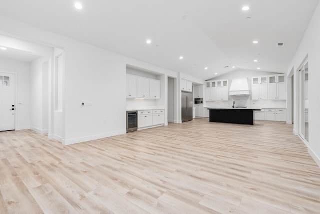 unfurnished living room with lofted ceiling, sink, beverage cooler, and light hardwood / wood-style floors