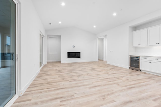 unfurnished living room with lofted ceiling, beverage cooler, indoor bar, and light hardwood / wood-style flooring