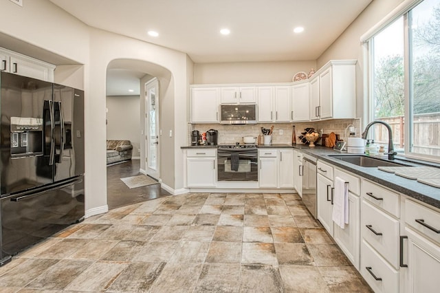 kitchen with sink, appliances with stainless steel finishes, white cabinetry, backsplash, and dark stone counters