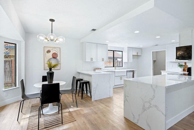 kitchen with stainless steel dishwasher, decorative light fixtures, kitchen peninsula, and white cabinets