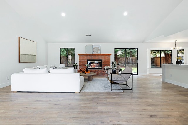 living room with a brick fireplace, a notable chandelier, light hardwood / wood-style floors, and high vaulted ceiling