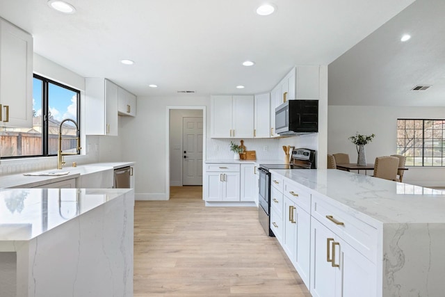 kitchen featuring appliances with stainless steel finishes, tasteful backsplash, white cabinetry, light stone counters, and light wood-type flooring