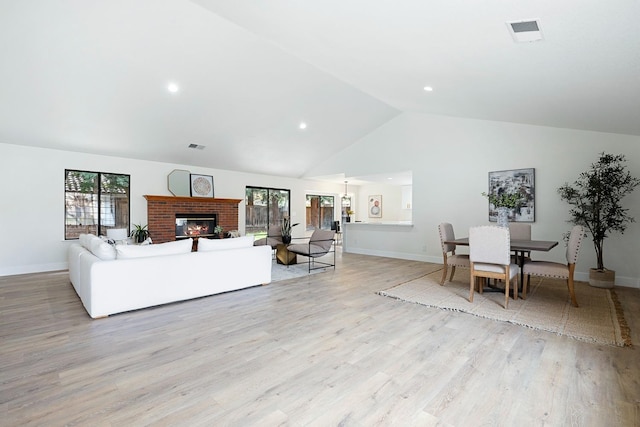 living room with high vaulted ceiling, a fireplace, and light hardwood / wood-style flooring